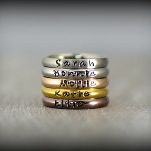 May include: Five stacked silver rings with different names engraved on them: Sarah, Bonnie, Mollie, Katie, and Ellie.