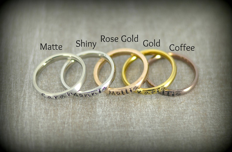 May include: Five rings in different finishes: matte silver, shiny silver, rose gold, gold, and coffee. Each ring has a different name engraved on it: "Sara", "Yvonne", "Mollie", "Katie", and "Ellie".