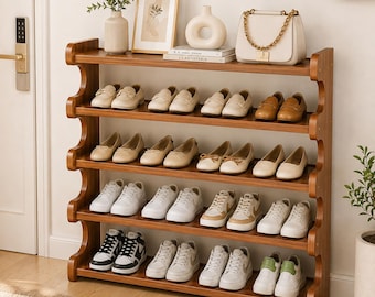 May include: A five-tier wooden shoe rack with curved side supports, holding various styles of footwear including loafers, flats, and sneakers. The top shelf displays a vase, a framed picture, a decorative ceramic object, and a white handbag.