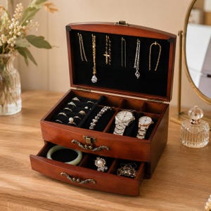 May include: A dark wood jewelry box with a hinged lid and a pull-out drawer. The interior features black velvet lining, hooks for necklaces, compartments for rings, and slots for two wristwatches. The exterior has ornate metal drawer pulls.