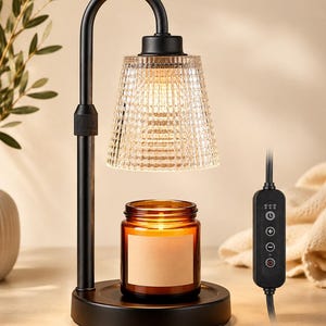 May include: A black metal candle warmer lamp with a curved arm and a textured, clear glass shade. The lamp features a circular base holding an amber glass candle jar with a blank label. A black corded controller with timer and brightness buttons.