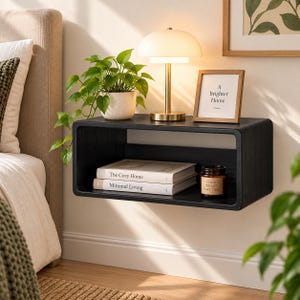 Puede incluir: Un estante de pared flotante rectangular negro con esquinas redondeadas. Encima hay una l&aacute;mpara blanca con base dorada, una planta verde en maceta y un marco con el texto A Brighter Home. Dentro del estante hay dos libros y una vela peque&ntilde;a.
