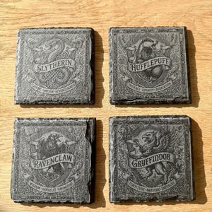 Pode incluir: Quatro porta-copos quadrados de ardósia com desenhos gravados dos quatro brasões: Slytherin com uma cobra, Hufflepuff com um texugo, Ravenclaw com uma águia e Gryffindor com um leão. Cada porta-copos inclui o nome e os traços da casa.