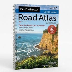 May include: A 2027 Rand McNally Large Scale Road Atlas with a spiral binding. The cover features a coastal landscape with a rocky cliff, green vegetation, and blue ocean water. Text includes 'Take the Road Less Traveled' and 'Top 27 Reasons to Travel'.