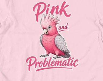 May include: A light pink t-shirt featuring a graphic illustration of a pink cockatoo bird. The text above the bird reads Pink and the text below the bird reads Problematic in a stylized pink font. The shirt has a crew neckline and short sleeves.