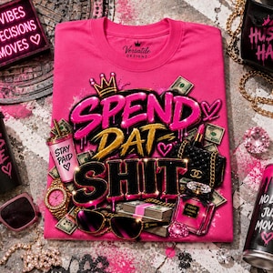 May include: A bright pink t-shirt featuring a graphic print with the text "SPEND DAT SHIT" in bold, stylized lettering, accompanied by illustrations of a crown, a pink cup labeled "STAY PAID," a gold watch, sunglasses, money, and perfume.