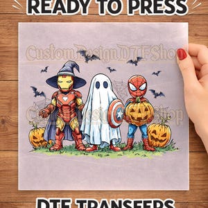 May include: A DTF transfer sheet featuring a cartoon illustration of three characters dressed for Halloween: Iron Man in a witch hat, a ghost holding a shield, and Spider-Man holding a jack-o'-lantern, surrounded by bats and pumpkins.