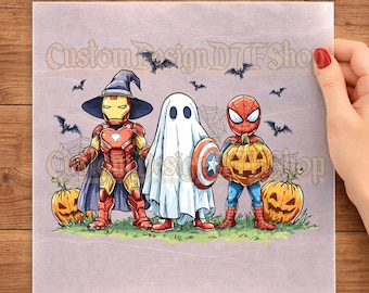 May include: A DTF transfer sheet featuring a cartoon illustration of three characters dressed for Halloween: Iron Man in a witch hat, a ghost holding a shield, and Spider-Man holding a jack-o'-lantern, surrounded by bats and pumpkins.