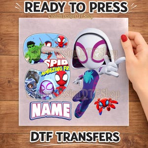 May include: A DTF transfer sheet featuring a large number three filled with Marvel Spidey and His Amazing Friends characters including Hulk, Spider-Man, and Ghost-Spider. Next to the number is a Ghost-Spider figure and a placeholder text box labeled NAME.
