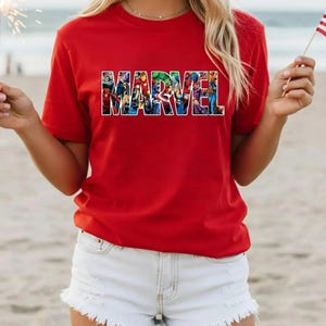 Peut inclure: Un t-shirt rouge &agrave; manches courtes avec le mot MARVEL imprim&eacute; en grandes lettres majuscules sur la poitrine. Les lettres sont remplies d'un collage graphique color&eacute; repr&eacute;sentant divers personnages de super-h&eacute;ros de bandes dessin&eacute;es.