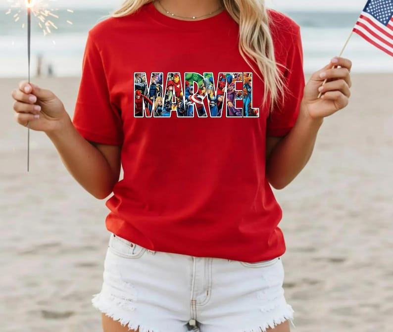 Peut inclure: Un t-shirt rouge &agrave; manches courtes avec le mot MARVEL imprim&eacute; en grandes lettres majuscules sur la poitrine. Les lettres sont remplies d'un collage graphique color&eacute; repr&eacute;sentant divers personnages de super-h&eacute;ros de bandes dessin&eacute;es.