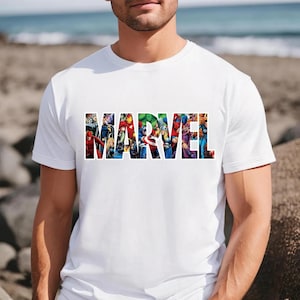Peut inclure: Un t-shirt blanc &agrave; manches courtes avec le mot MARVEL &eacute;crit en grandes lettres capitales. L'int&eacute;rieur de chaque lettre contient une illustration graphique color&eacute;e de divers personnages de bandes dessin&eacute;es, incluant des super-h&eacute;ros.