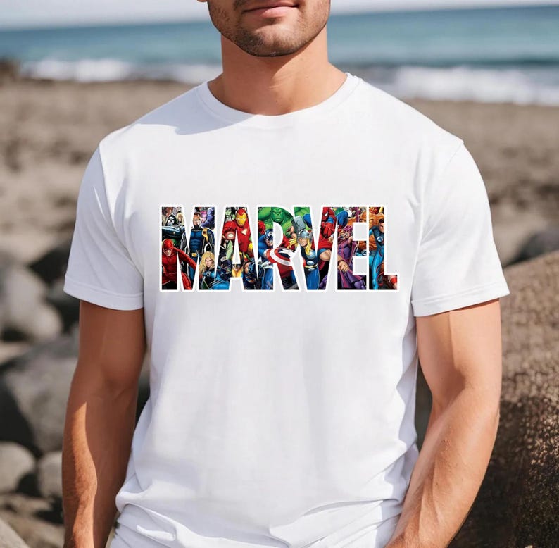 Peut inclure: Un t-shirt blanc &agrave; manches courtes avec le mot MARVEL &eacute;crit en grandes lettres capitales. L'int&eacute;rieur de chaque lettre contient une illustration graphique color&eacute;e de divers personnages de bandes dessin&eacute;es, incluant des super-h&eacute;ros.