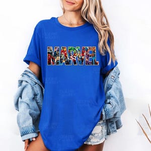 Peut inclure: Un t-shirt bleu roi &agrave; manches courtes avec le mot MARVEL imprim&eacute; en grandes lettres majuscules sur la poitrine. Les lettres sont remplies d'un collage color&eacute; repr&eacute;sentant diverses illustrations de personnages de bandes dessin&eacute;es Marvel.