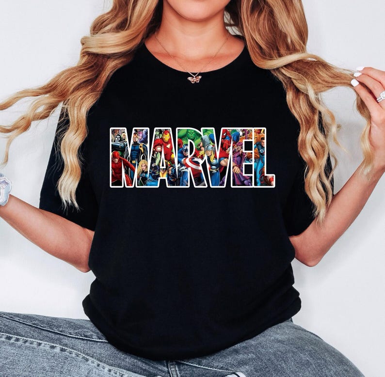 Peut inclure: Un t-shirt noir &agrave; manches courtes avec le mot MARVEL &eacute;crit en grandes lettres blanches. &Agrave; l'int&eacute;rieur de chaque lettre se trouve une illustration graphique color&eacute;e de divers personnages de bandes dessin&eacute;es, dont Iron Man, Hulk, Thor et Captain America.