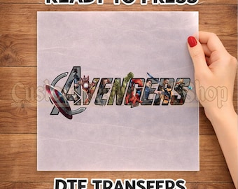 May include: A square DTF transfer sheet featuring the Avengers logo with various superhero characters integrated into the lettering. The text READY TO PRESS is printed above the design, and DTF TRANSFERS is printed below the design on a light background.