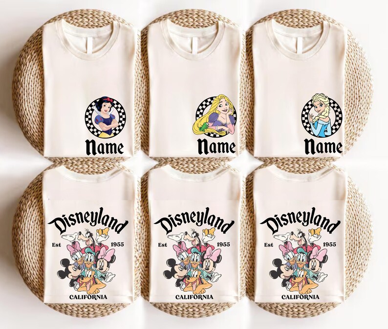Puede incluir: Camisetas de color crema con gr&aacute;ficos de personajes de Disney, incluyendo Blancanieves, Rapunzel y Elsa, cada uno en un c&iacute;rculo a cuadros con la palabra "Name" debajo. Las camisetas inferiores presentan un gr&aacute;fico de Disneyland con el texto "Est 1955 CALIFORNIA."