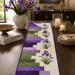 May include: A rectangular table runner featuring a patchwork design of purple and green fabric strips on one side and a cream-colored background on the other. The cream section is decorated with a vertical row of four printed purple iris flowers.