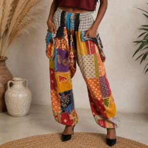 May include: Loose-fitting pants featuring a patchwork design with various colorful fabric patterns including red, yellow, orange, and blue. The pants have an elastic waistband, a drawstring, and two large side pockets with visible stitching details.