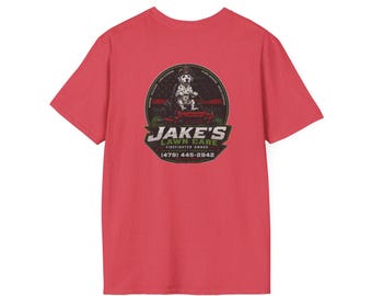 May include: A red short-sleeved t-shirt featuring a circular graphic on the back. The graphic depicts a Dalmatian dog wearing a firefighter helmet on a red lawn mower, with the text JAKE'S LAWN CARE, FIREFIGHTER OWNED, and (479) 445-2942.
