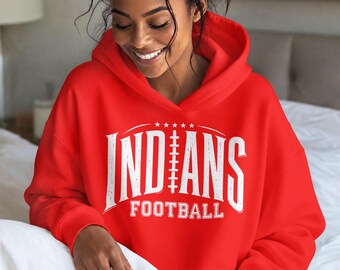 May include: A bright red hooded sweatshirt featuring white distressed-style lettering on the chest. The graphic displays the word INDIANS with a football lace design replacing the letter A, and the word FOOTBALL printed in smaller text below.