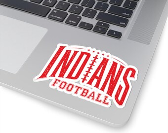 May include: A white sticker with a red distressed graphic featuring the text INDIANS with a football lace design replacing the letter I and the word FOOTBALL underneath. The sticker is applied to the surface of a silver laptop keyboard area.