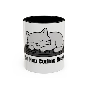 May include: White ceramic mug with a black interior. It features a gray cartoon cat sleeping on a keyboard, with the text "Cat Nap Coding Break" printed around the base.
