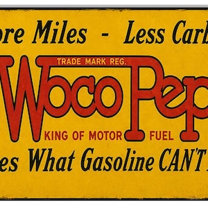 May include: A rectangular metal sign with a yellow background and black border. The text reads: More Miles - Less Carbon, Woco Pep, TRADE MARK REG., KING OF MOTOR FUEL, and Does What Gasoline CAN'T Do! The lettering is in red and black.