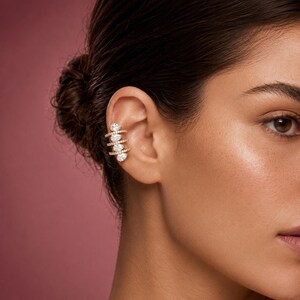 May include: A gold-toned ear cuff featuring four horizontal bands, each set with a single pear-shaped clear stone. The bands are connected by a vertical bar, creating a layered, multi-row appearance that wraps around the outer edge of the ear.