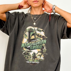 Peut inclure: T-shirt gris fonc&eacute; avec un graphisme de la s&eacute;rie Star Wars, "The Mandalorian and Grogu". Le motif comprend le casque du Mandalorien, Grogu et la phrase "This is the Way" en blanc et vert. Le t-shirt a des manches courtes.