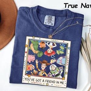 May include: A True Navy short-sleeve t-shirt featuring a square graphic print of various animated characters from Toy Story. The print includes the text "YOU'VE GOT A FRIEND IN ME" at the bottom. The shirt has a crew neckline and a Comfort Colors label.