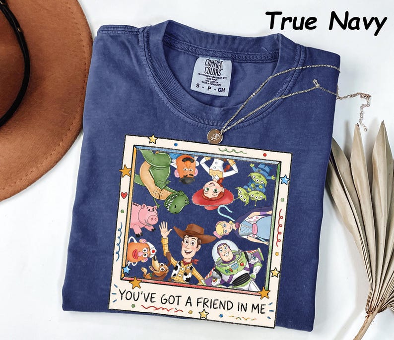 May include: A True Navy short-sleeve t-shirt featuring a square graphic print of various animated characters from Toy Story. The print includes the text "YOU'VE GOT A FRIEND IN ME" at the bottom. The shirt has a crew neckline and a Comfort Colors label.