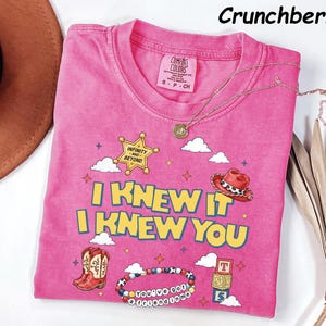 May include: A pink short-sleeve t-shirt featuring a graphic print with the text I KNEW IT I KNEW YOU, a sheriff star labeled INFINITY AND BEYOND, a cowboy hat, boots, a beaded bracelet with the text YOU'VE GOT A FRIEND IN ME, and alphabet blocks.