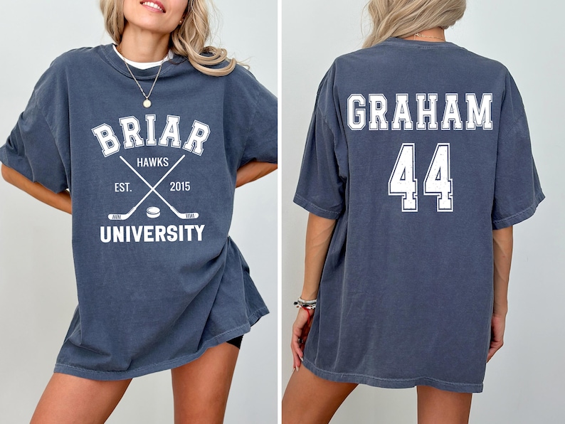 May include: A dark blue t-shirt with white text and graphics. The front features "Briar Hawks University" with crossed hockey sticks and the year "2015." The back displays "Graham" and the number "44."
