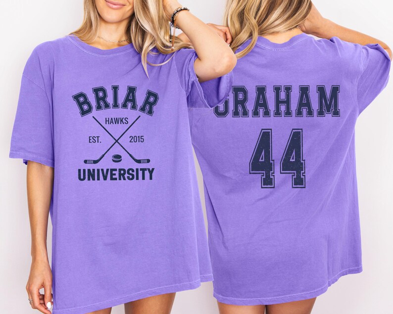 May include: A lilac-colored t-shirt with the text "BRIAR HAWKS UNIVERSITY" and crossed hockey sticks. The back of the shirt displays the name "GRAHAM" and the number "44" in navy blue.