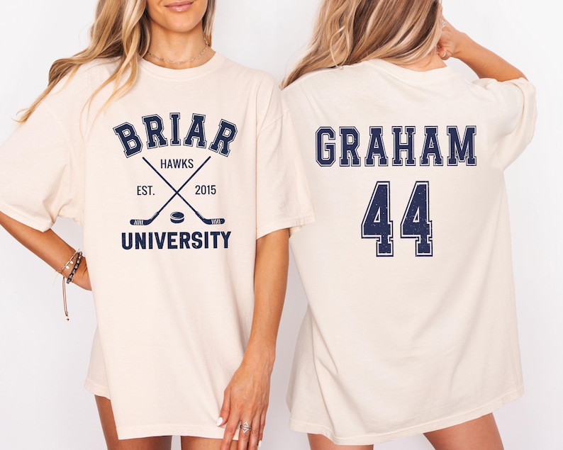 May include: Cream-colored t-shirt featuring the text "BRIAR HAWKS UNIVERSITY" with crossed hockey sticks and the year 2015. The back of the shirt displays "GRAHAM 44" in navy blue lettering.
