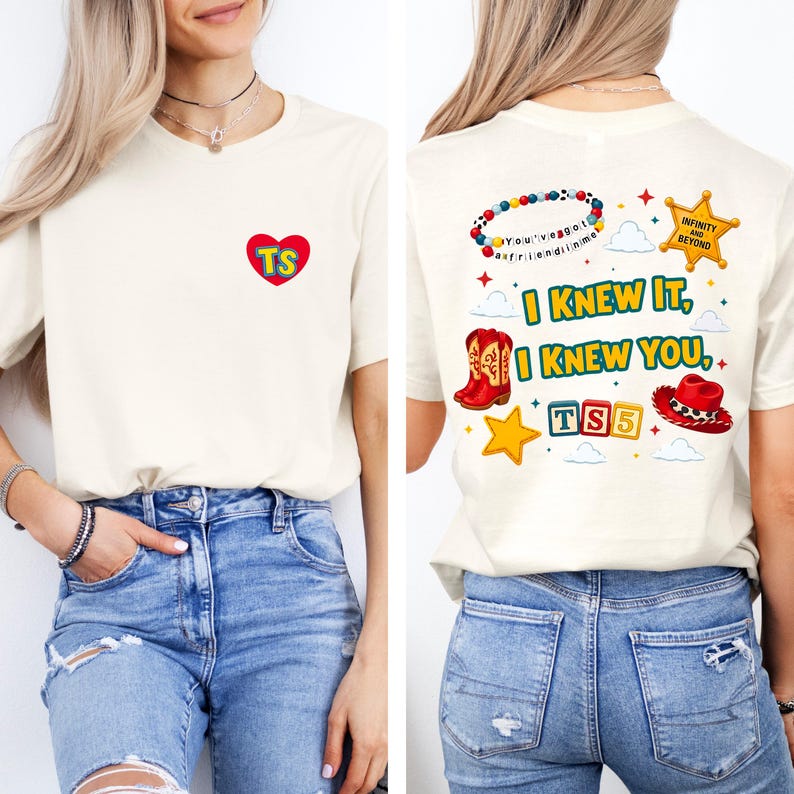 May include: A cream-colored t-shirt featuring a small red heart with yellow TS letters on the front. The back displays a colorful graphic with a beaded bracelet, a sheriff star, red cowboy boots, a red hat, and the text I KNEW IT, I KNEW YOU.