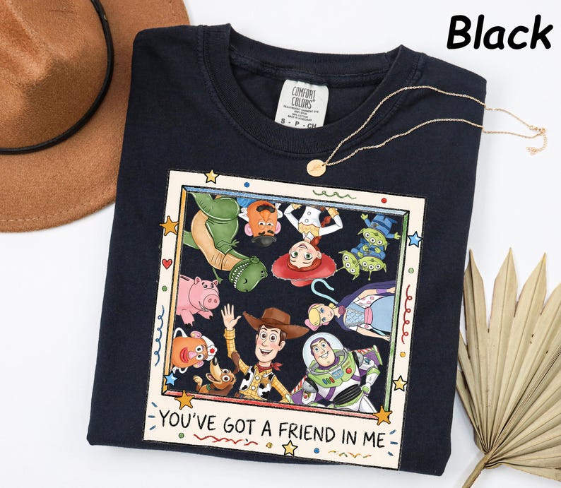 May include: A black t-shirt featuring a square graphic print of various animated characters from Toy Story arranged in a frame. The text "YOU'VE GOT A FRIEND IN ME" is printed at the bottom of the frame. The shirt has a white neck label.