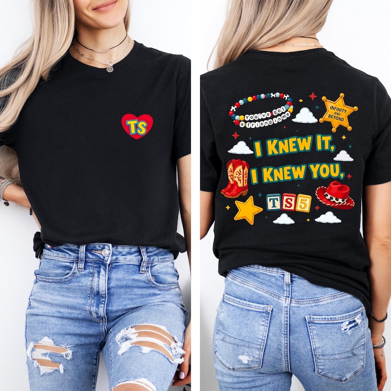 May include: A black t-shirt featuring a small red heart on the front with the letters TS. The back displays a colorful graphic with the text I KNEW IT, I KNEW YOU, TS5, and INFINITY AND BEYOND, alongside illustrations of cowboy boots, a hat, and a star.