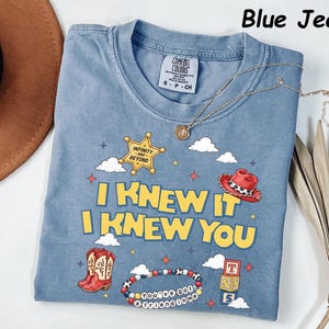 May include: A blue jean colored t-shirt featuring a graphic print with a yellow sheriff star labeled Infinity and Beyond, a red cowboy hat, red cowboy boots, a beaded bracelet with the text You've Got a Friend in Me, and blocks with letters.