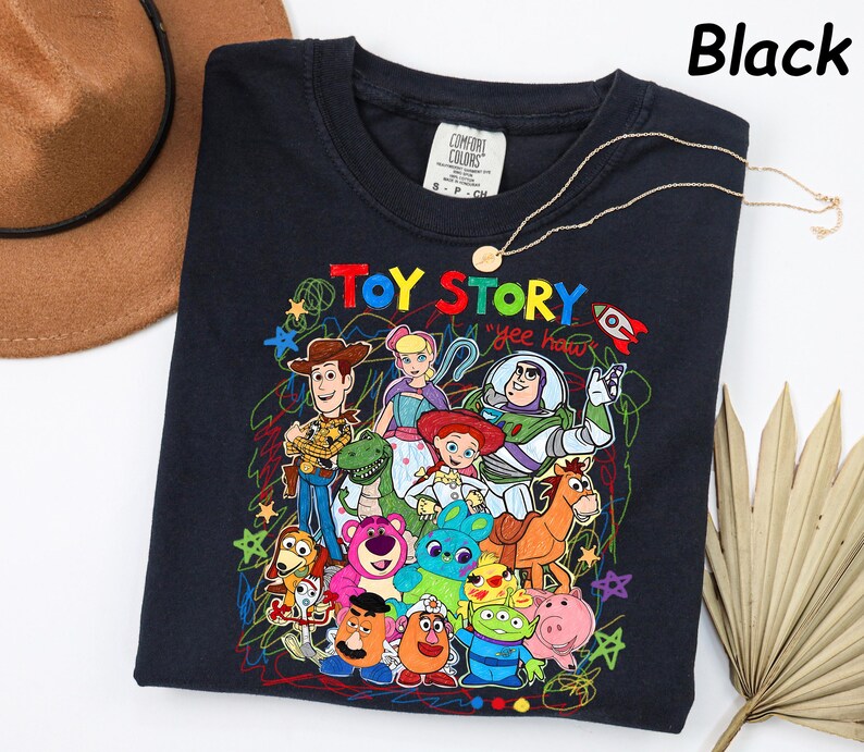 May include: Black crew neck sweatshirt featuring a colorful graphic of Toy Story characters. The design includes Woody, Buzz Lightyear, and other characters from the animated film. A gold necklace is draped across the sweatshirt.