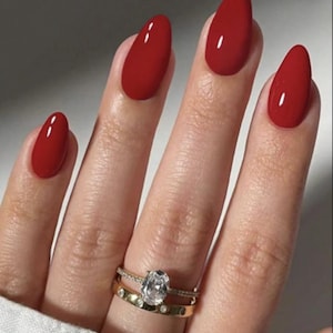 Può includere: Un set di due anelli in oro indossati su un dito. L'anello superiore presenta una pietra centrale trasparente a taglio ovale con una fascia pavé, mentre l'anello inferiore è una fascia in oro massiccio con piccole pietre chiare distanziate.