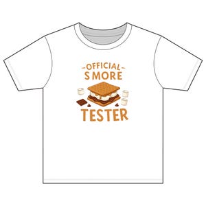 May include: White t-shirt featuring a graphic of a s'more, chocolate, and marshmallows. The text "OFFICIAL S'MORE TESTER" is printed in brown. The design is centered on the front of the shirt.