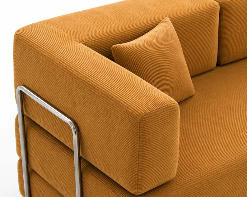 May include: A mustard yellow corduroy sofa featuring a textured ribbed fabric surface, a matching square throw pillow, and a polished silver-toned metal frame that supports the armrest and side structure of the furniture piece.