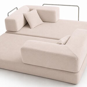 May include: A light beige corduroy modular sofa featuring a low-profile design with two rectangular backrests, two matching throw pillows, and a thin metallic frame structure that wraps around the perimeter of the seating area.