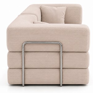 May include: A beige corduroy sofa featuring a modular design with three stacked horizontal cushion sections. The structure is supported by a prominent, U-shaped brushed metal frame that wraps around the side of the sofa, providing a distinct industrial contrast to the soft, textured fabric of the upholstery.