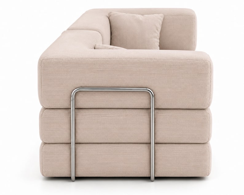May include: A beige corduroy sofa featuring a modular design with three stacked horizontal cushion sections. The structure is supported by a prominent, U-shaped brushed metal frame that wraps around the side of the sofa, providing a distinct industrial contrast to the soft, textured fabric of the upholstery.
