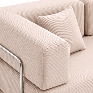 May include: A light beige sofa upholstered in a textured corduroy fabric featuring horizontal ribbed lines. The sofa includes a matching square throw pillow and is supported by a polished silver-toned metal frame visible on the side armrest.