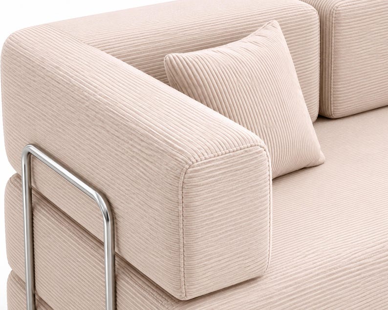 May include: A light beige sofa upholstered in a textured corduroy fabric featuring horizontal ribbed lines. The sofa includes a matching square throw pillow and is supported by a polished silver-toned metal frame visible on the side armrest.