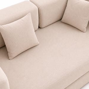 May include: A beige corduroy sofa featuring a textured, ribbed fabric surface. The furniture includes two matching square throw pillows placed on the seat, with thick, padded armrests and a continuous, uniform fabric finish across all visible parts.